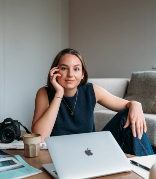 Social media manager terwijl ze werkt aan social media strategie en content creatie, met camera en laptop op tafel.